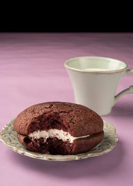 Black raspberry whoopie pie on a plate with a bite taken out.